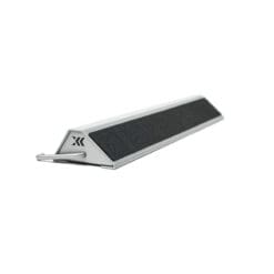 The Exxentric kBox4 Foot Block is a triangular metal doorstop featuring a textured black strip on top, a hook at one end, and a minimalist design.