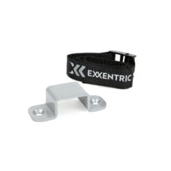 The Exxentric kBox4 Floor Attachment includes a metal bracket with two holes and a black adjustable strap displaying EXXENTRIC and a stylized logo in white, featuring a buckle for fastening.