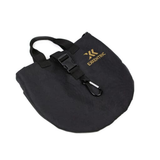 The Exxentric Flywheel Bag is a black fabric bag with EXXENTRIC in gold, a handle, buckle clasp, carabiner clip on the front, and a rounded bottom.